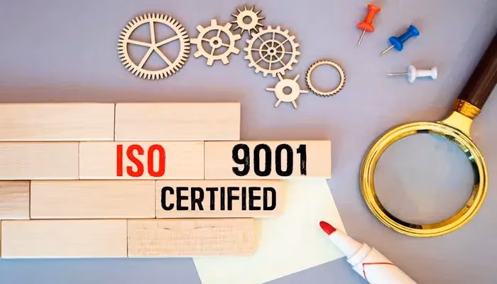 Blocks spelling "ISO 9001 Certified," surrounded by gears, push pins, and a magnifying glass, symbolizing ISO 9001 document control.
