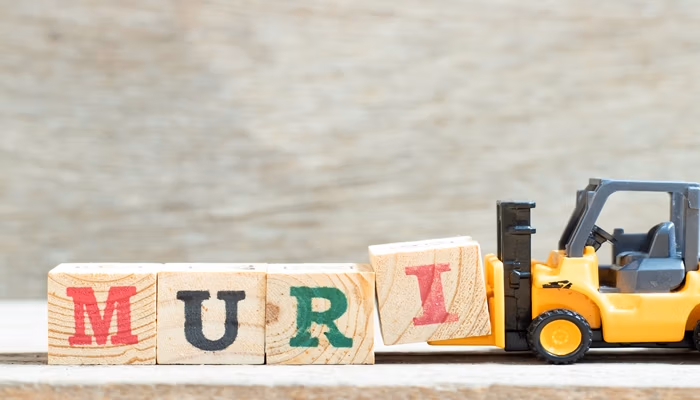 A toy forklift attempts to lift wooden blocks spelling "MURI," representing the concept of Muri in Lean manufacturing, which refers to overburdening resources.