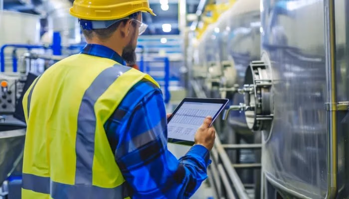 Engineer inspecting machinery with EPEI (Every Part Every Interval) system on tablet in industrial facility