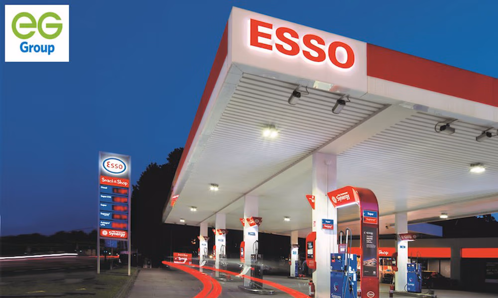 A brightly lit Esso gas station at dusk, showing fuel pumps and signage, suitable for a gas station inspection.